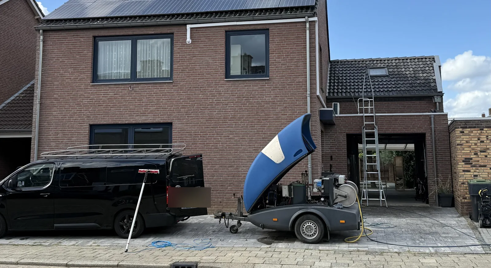 De bus en de hogedrukunit van JANA voor een woning, ladder tegen de garage